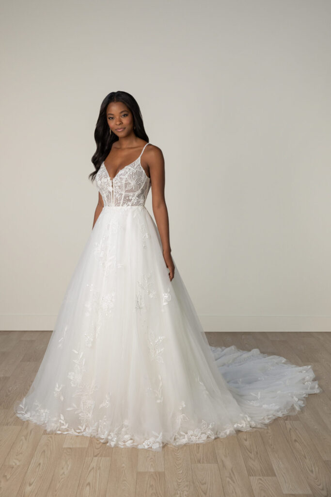 Stella York-8017-Pure Bridal-Both glamorous and romantic, Style 8017 is an allover lace ballgown wedding dress that is a dream come true for the princess-at-heart. Delicate sparkling spaghetti straps gracefully flow into a sheer bodice, featuring a soft V-neckline and daring plunging accent lined with illusion tulle for a subtle, sexy touch. The bodice showcases the stunning embellished embroidered lace adorned with shimmering sequins and beaded accents. From the waist, scattered floral lace appliqus dance across layers of soft tulle, creating an enchanting ballgown silhouette. For a blend of timeless elegance and contemporary glamour, this princess ballgown wedding dress is an absolute show-stopper for the romantic bride-edmonton bridal shop