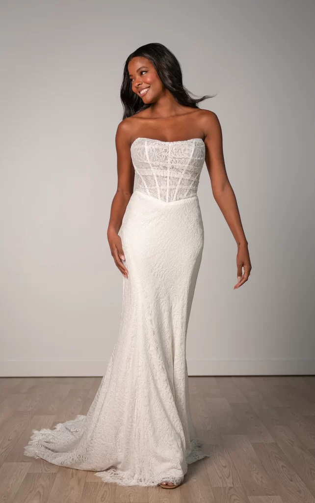 8086-Stella York-Pure Bridal, Edmonton bridal shop, Edmonton wedding dress. For the modern romantic bride, Style SY8086 dazzles as a sultry column wedding gown that blends charm and elegance in a breathtaking design. The bodice features a sheer corset-style construction with exposed boning, layered with delicate ruched tulle for a soft ethereal look. An intricate Chantilly lace underlayer elevates the gown, with the sculpted basque waist flowing seamlessly into a luxurious column skirt that gracefully hugs the body's curves. This gown is also available in plus sizes.
