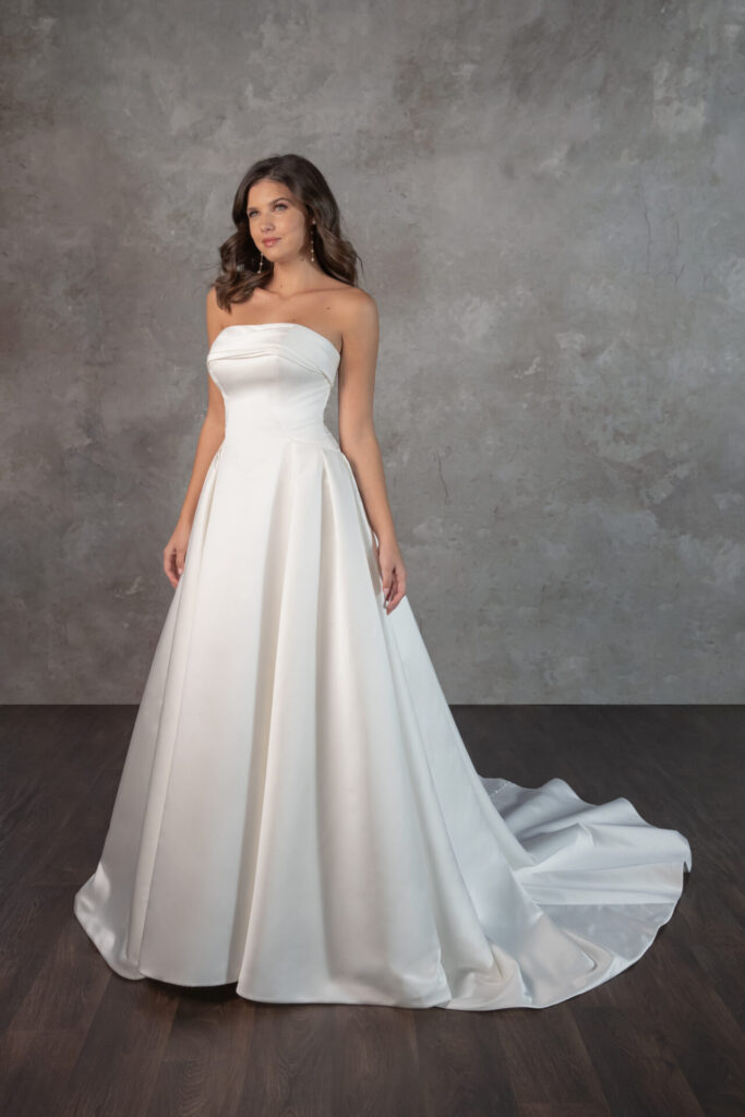 Pure Bridal-Essense of Australia-D4304-Edmonton Bridal Shop-Designed for the modern romantic, Style D4304 is a stunning satin ballgown that blends timeless elegance with contemporary charm. The strapless, straight-across neckline folds over a structured bodice, creating a refined yet effortlessly chic silhouette. Subtle seaming contours the figure before meeting the voluminous pleated skirt at the hips, delivering a regal statement. In the back, a row of fabric-covered buttons traces the length of the gown, adding a classic touch. With its grand yet minimalist appeal, this wedding dress is the ideal choice for the fashion-forward bride seeking sophistication with a hint of drama. This gown is also available in plus sizes.
