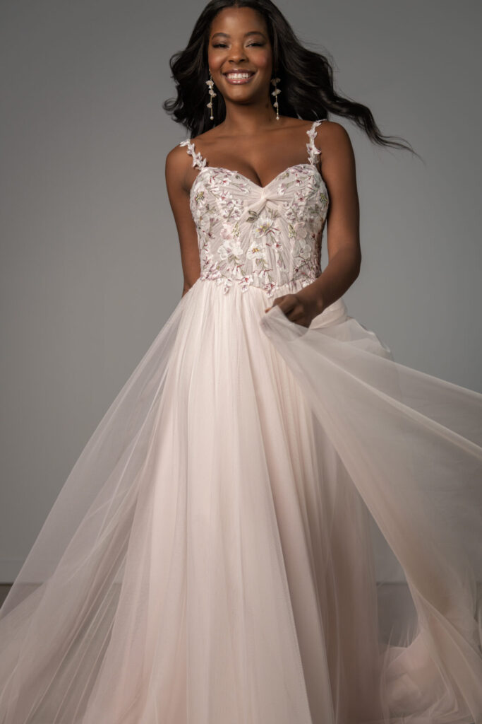 Pure Bridal-Stella York-8113-Capturing the essence of romantic bridal fashion, Style SY8113 enchants with its soft A-line silhouette and ethereal, colorful embroidered lace. Delicate, petal-adorned spaghetti straps lead to a deep sweetheart neckline, where a sheer bodice features a stunning twisted ruched knot detail. A subtly scooped back adds a hint of allure, while layers of frothy pink tulle cascade into a soft A-line skirt, creating a dreamy, weightless effect. This enchanting dress is a breathtaking blend of whimsy and elegance for the bride who embraces playful romance. This gown is also available in plus sizes and with a variety of bodice lining options.